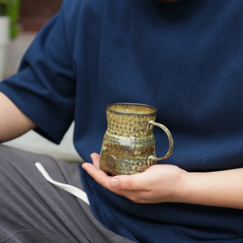 Lifestyle view of a hand-pinched iron clay ceramic mug with Green Shell Glaze held in hand